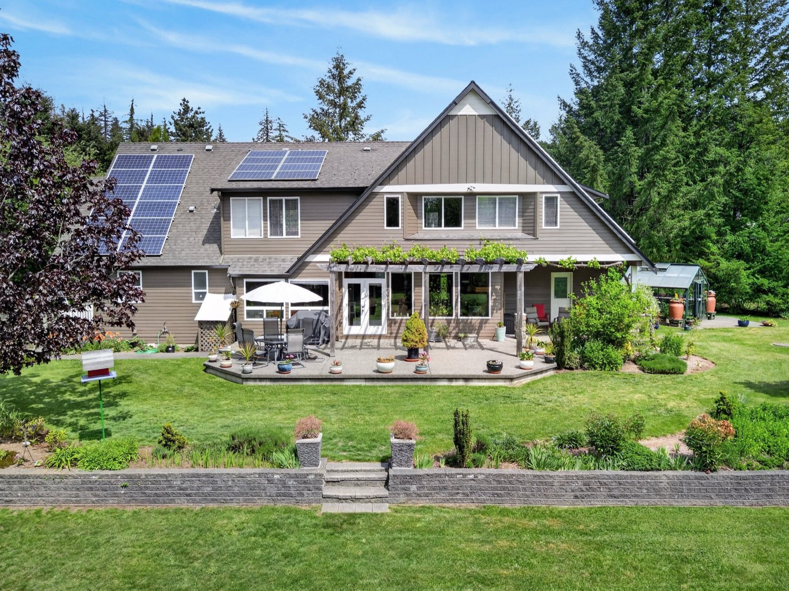Aerial view of a home with solar panels, patio and gardens