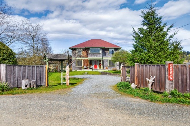 Two-storey country home with a red metal roof at the end of a gravel drive
